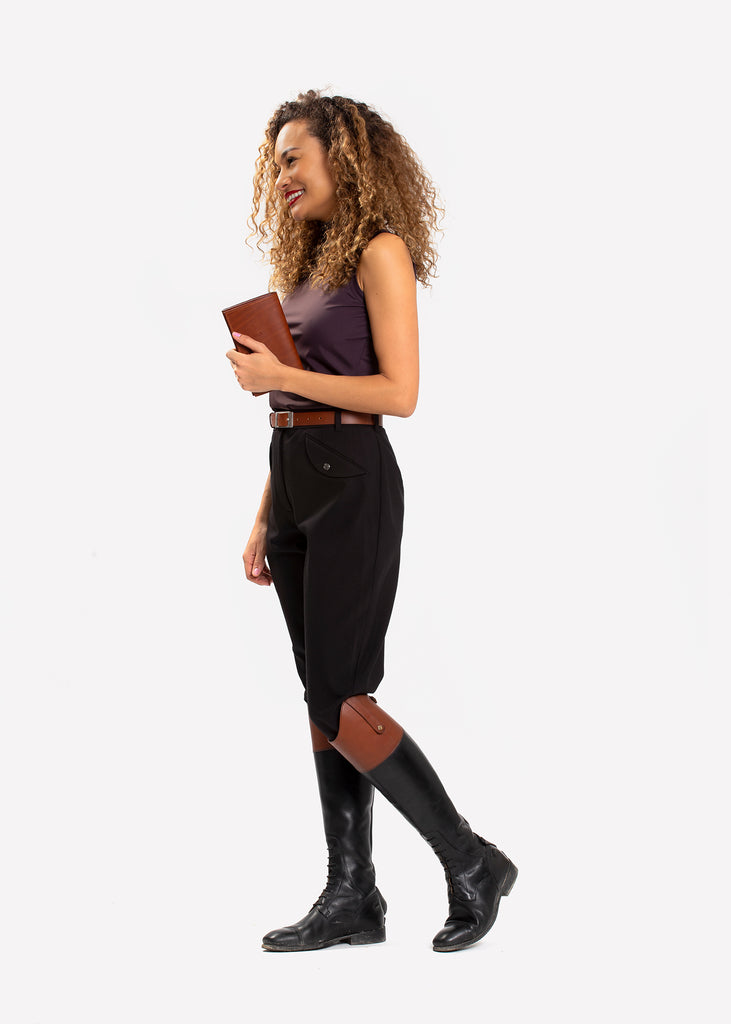 Female model in black breeches and boots holding a small brown leather bag