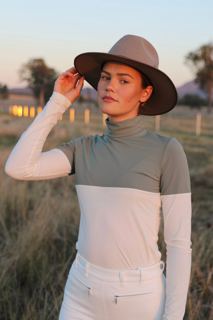 Woman in a hat standing on a field dressed in white looking in to the camera