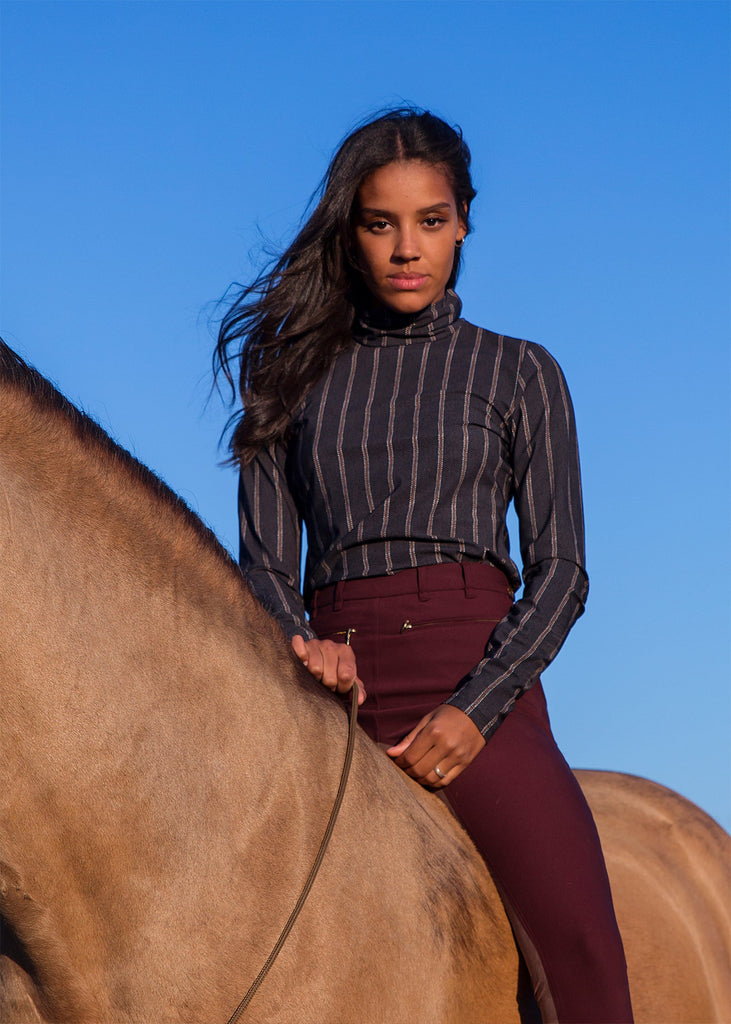 Woman in striped turtle neck top sitting on a horse and looking directly in to the camera