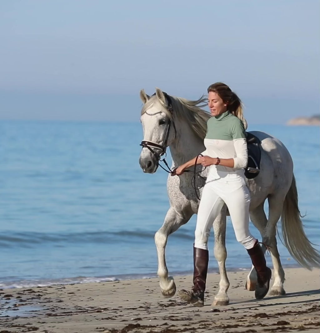 Blonde woman in white full seat riding breeches with her white horse. 