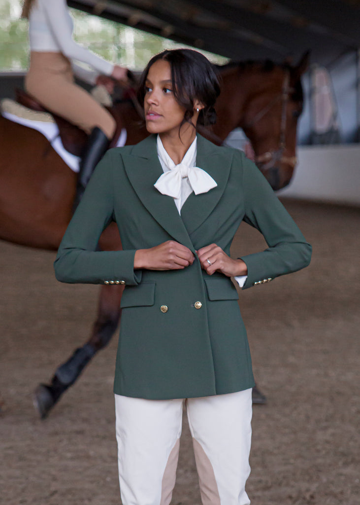 Model in front of a horse buttoning a green horse riding show jacket. 