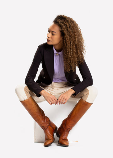 Female model wearing an unbuttoned horse riding jacket in black. 