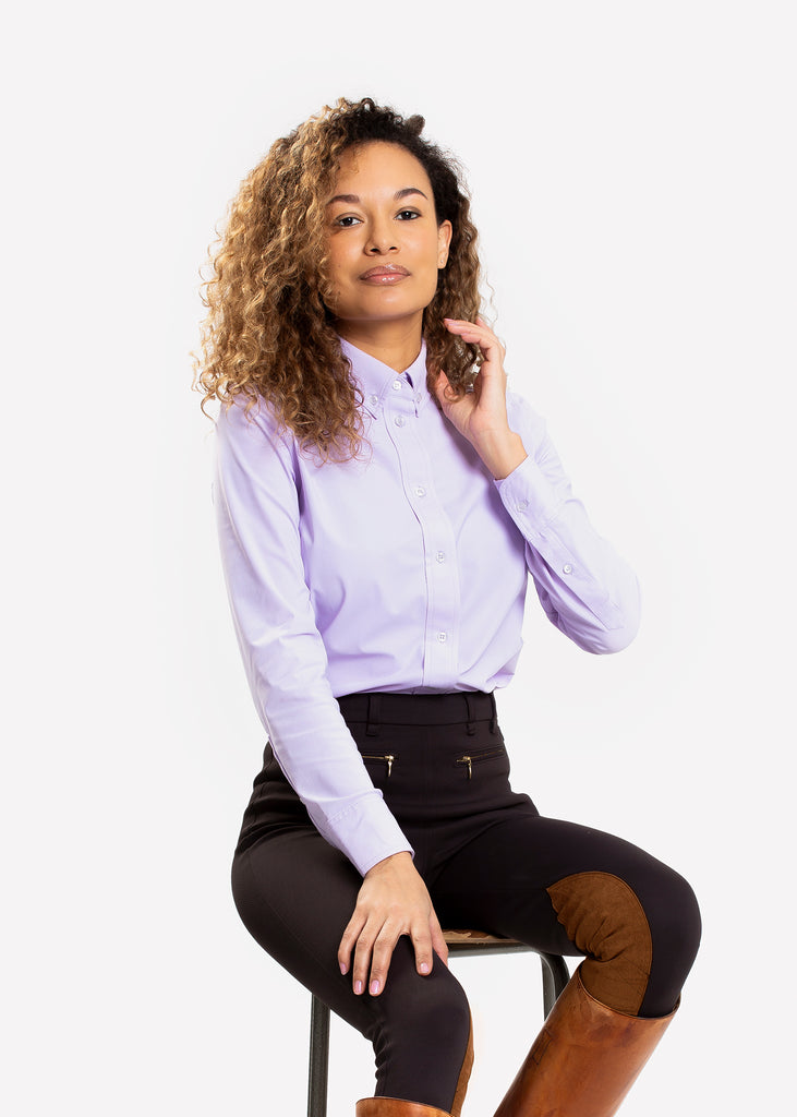 Female model sitting on a chair in a classic tailored button down shirt in lilac. 