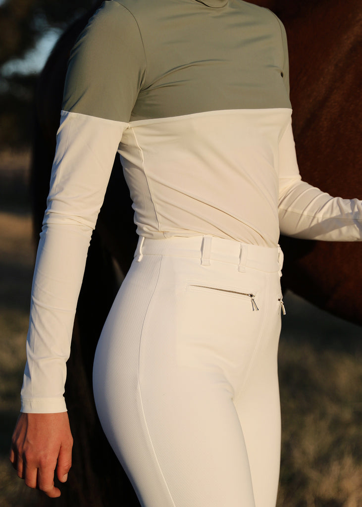 Model wearing white full seat riding breeches and a color block top. 