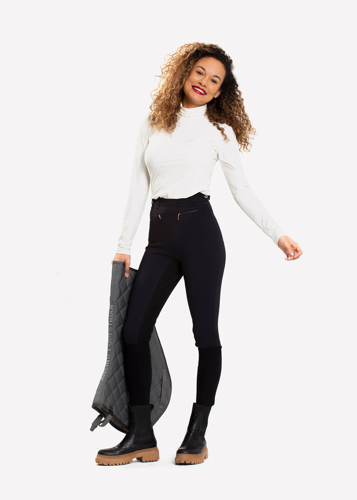 Female model in black high waist breeches holding a saddle pad in her hand. 