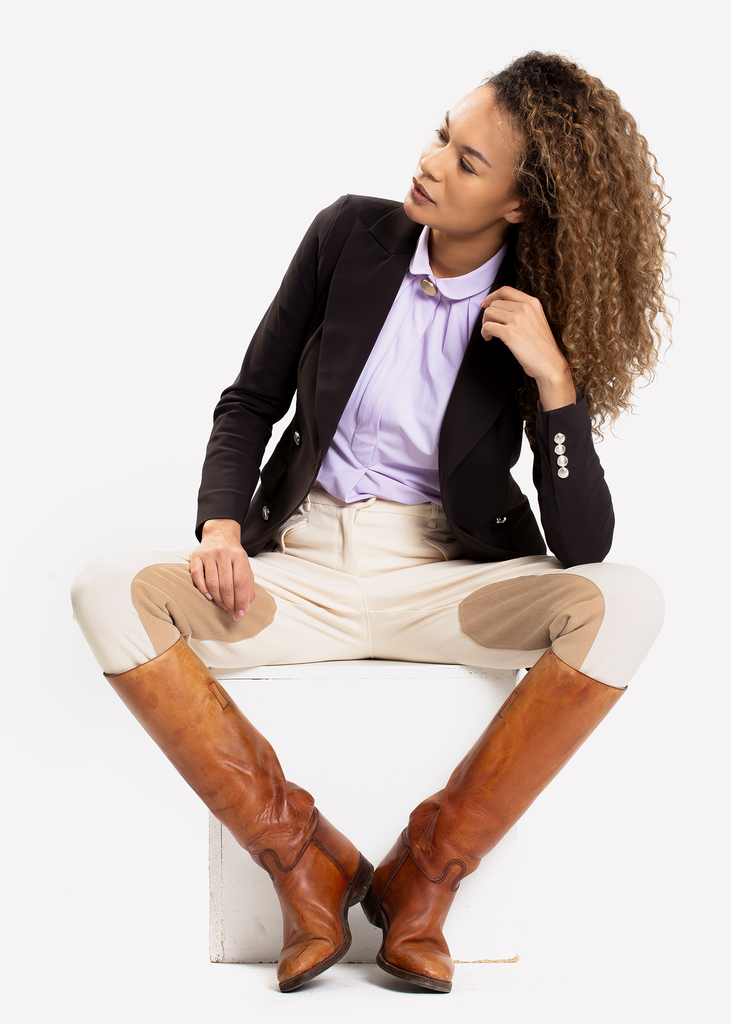 Young woman sitting on a white box wearing white breeches and dark open blazer