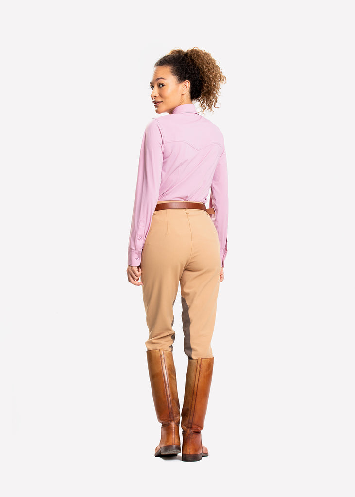Female model in pink shirt, beige breeches and brown riding boots looking over her shoulder