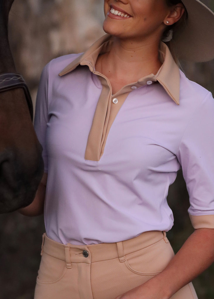 Smiling woman dressed in a lilac/tan shirtsleeve shirt next to a horse