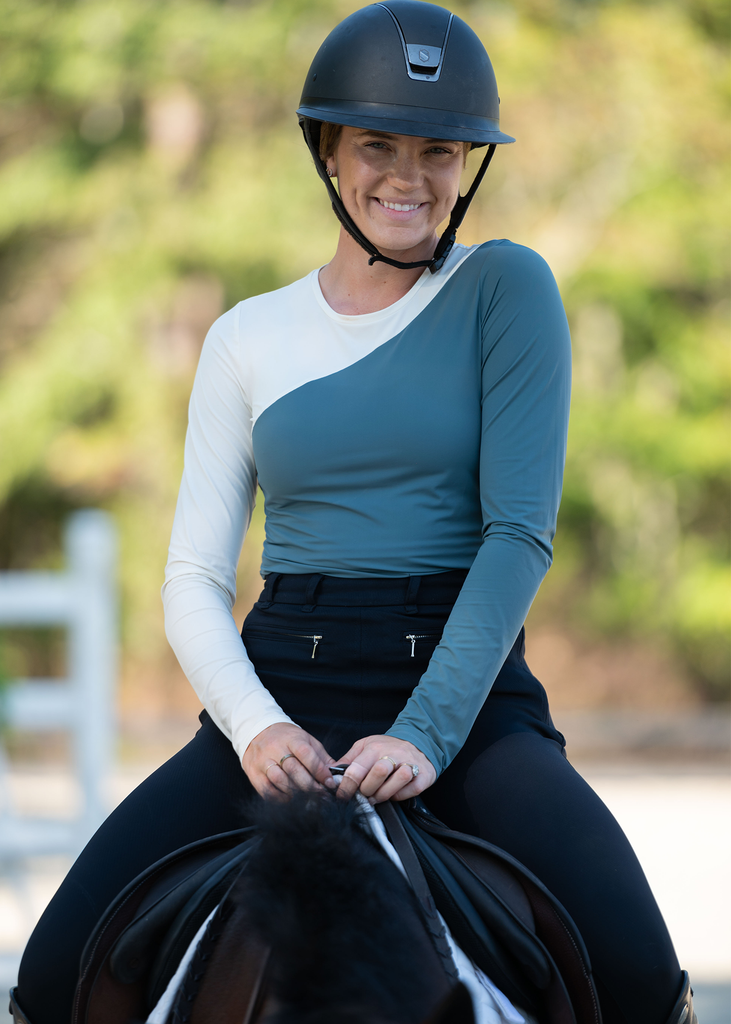 Smiling woman on a horse wearing helmet, a color blocket top and black breeches