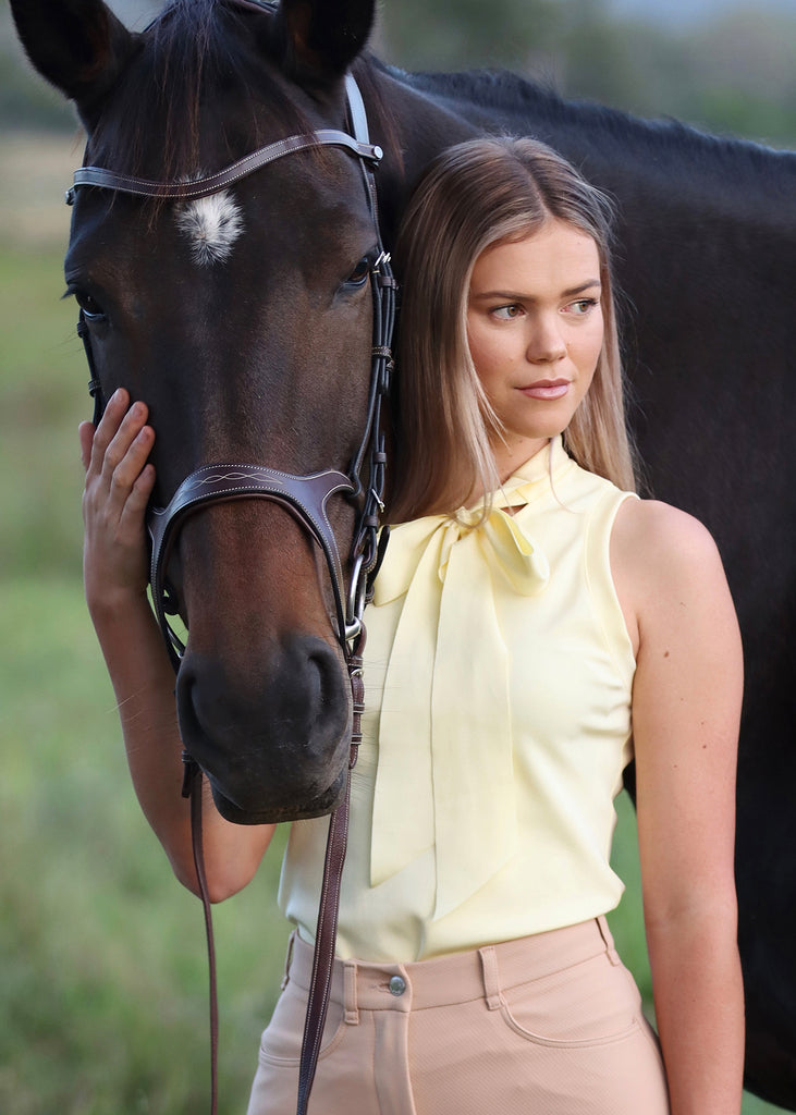 Close up on a woman in yellow bow blouse standing close to a horse