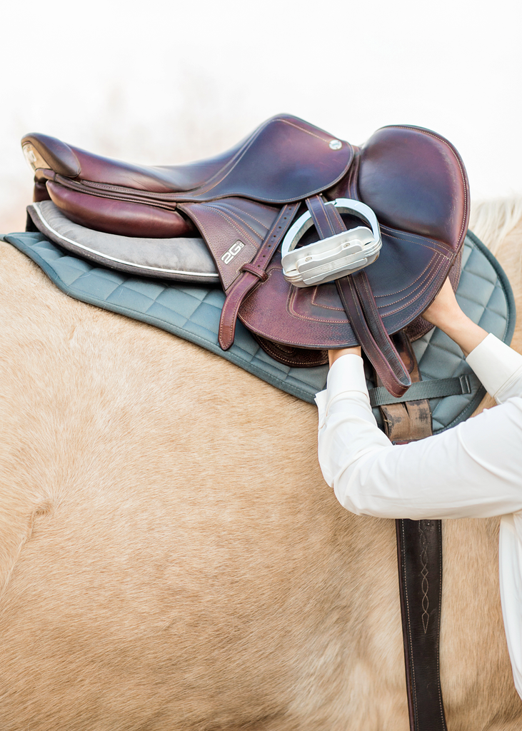 Saddle with a green jump saddle pad on a palomino horse