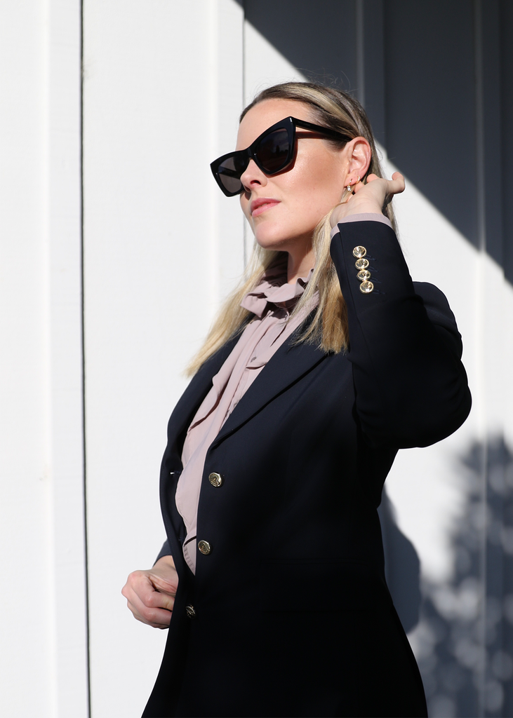 Blonde woman in sunglasses wearing a navy blazer with a lilac blouse